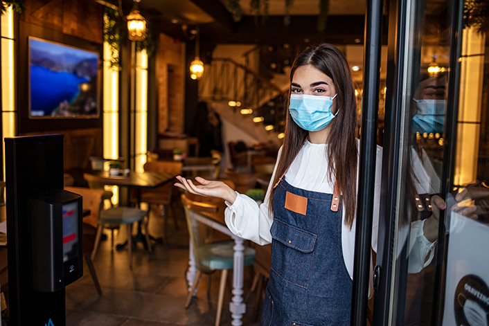A restaurant hostess with a mask on welcoming the viewer in